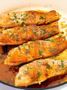 three fish fillets in a pan with sauce and garnishes on the side