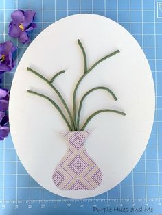 purple flowers are in a vase on a cutting board next to blue and white paper