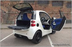 an electric car with its doors open in a parking lot next to a brick wall