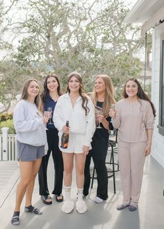 four women standing on the porch holding wine glasses