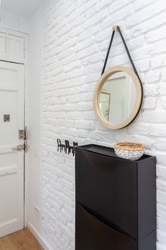 a white brick wall with a black cabinet and mirror on the front door, next to a wooden floor