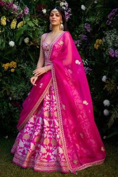 a woman wearing a pink and yellow lehenga with flowers in the back ground