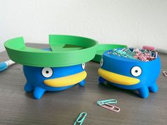 two blue birds with green beaks sitting on a table next to paper clips and scissors