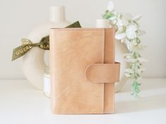 a small tan leather journal with a bow on the front, sitting next to a white vase