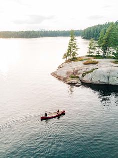 two people in canoes paddling on the water near an island with pine trees