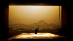 a man standing in front of a window looking out at the mountains and city below