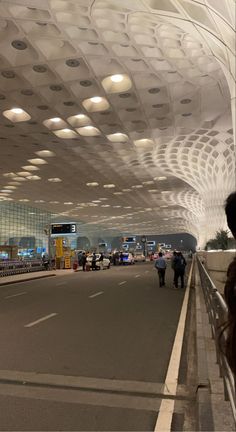 people are walking through an airport terminal with lights on the ceiling and overhead lighting above them