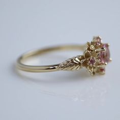 a yellow gold ring with an oval pink tourmaline surrounded by leaves and flowers