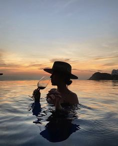 a woman holding a wine glass in her hand while standing in the water at sunset