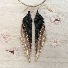 a pair of black and gold beaded earrings sitting on top of a wooden table