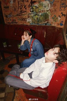 two people sitting on a red couch in a room with graffiti all over the walls