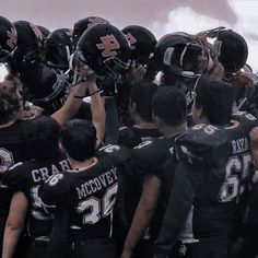 a group of football players standing next to each other with helmets on their heads and hands in the air