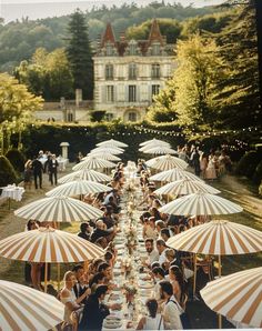 a group of people sitting under umbrellas in front of a large building with lots of tables