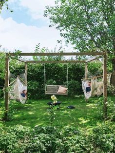 two people laying in hammocks on the grass near some trees and bushes,