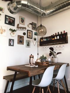 a dining room table with chairs and pictures on the wall above it, along with hanging wine bottles