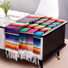 a multicolored blanket sitting on top of a white table next to a vase with flowers