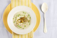 a white bowl filled with soup on top of a yellow plate next to a spoon