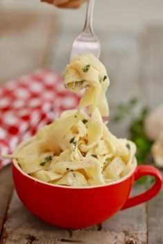 a spoon full of pasta being lifted from a red bowl