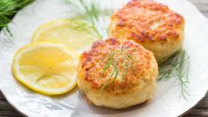 two crab cakes on a white plate with lemon wedges and rosemary garnish