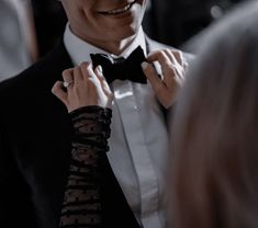 a man in a tuxedo adjusts his tie while another woman looks on