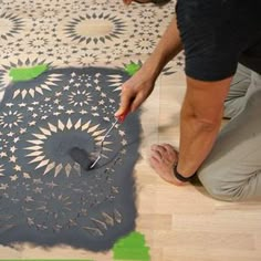 a man is painting the floor with black and white designs on it, while another person holds a paintbrush in their hand