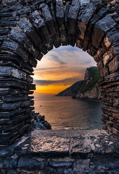 the sun is setting through an arch in a stone wall by the ocean with rocks on either side