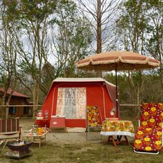 a red tent set up in the woods with chairs and an umbrella