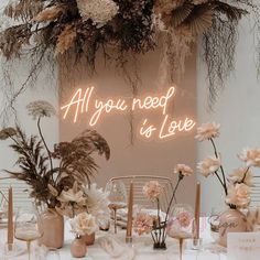 a table topped with lots of flowers next to a neon sign that says treat yourself