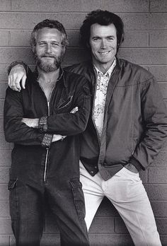 two men standing next to each other in front of a brick wall