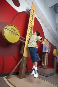 a young boy climbing on a giant wooden ruler in a play area at the children's museum