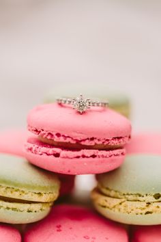 pink and green macaroons stacked on top of each other with a diamond ring