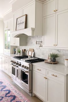 a kitchen with white cabinets, an oven and a pink rug on the floor in front of it