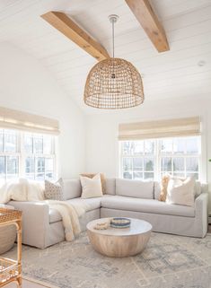 a living room with white furniture and wood beams in the ceiling, along with large windows