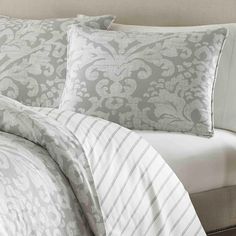 a bed with white and grey comforters on top of the headboard in a bedroom