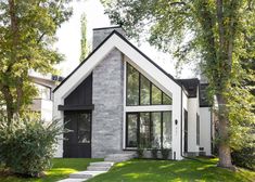 a white and black house with trees in the front yard, grass on the lawn