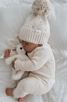 a baby is laying down with a stuffed animal and wearing a white knitted outfit