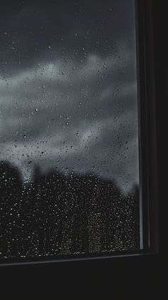 rain drops on the window and trees in the background with dark clouds behind it as seen from outside