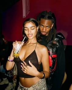 a man and woman standing next to each other at a nightclub with drinks in their hands