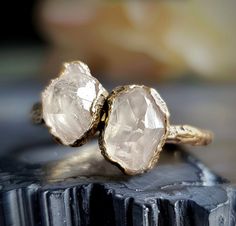 two gold rings with large white stones on top of each other in front of a black piece of wood