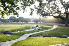 a grassy field with a small creek running through it and a person sitting on a bench in the distance