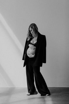 a woman holding a baby in her arms while standing next to a wall with the light shining on her