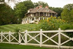 a white picket fence in front of a large house with sunflowers on the lawn