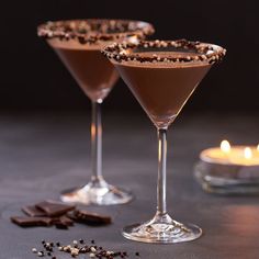 two martini glasses filled with chocolate and sprinkles next to a lit candle