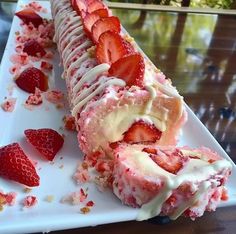 a long piece of cake with strawberries on it sitting on a white platter