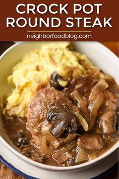 a white bowl filled with meat and mushrooms covered in gravy on top of a wooden table