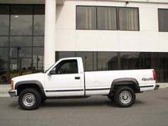 a white pick up truck parked in front of a large building with windows on it