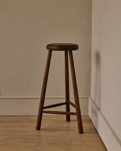 a wooden stool sitting on top of a hard wood floor next to a white wall