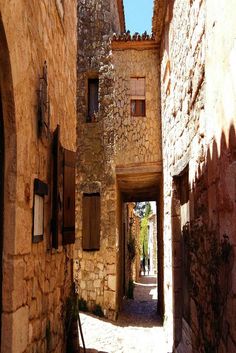 an alley way with cobblestone stone buildings and shutters on both sides, leading to another building