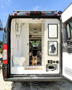 a small dog sitting in the back of a white van with its door open and pictures on it