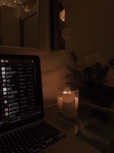 an open laptop computer sitting on top of a desk next to a candle and flowers